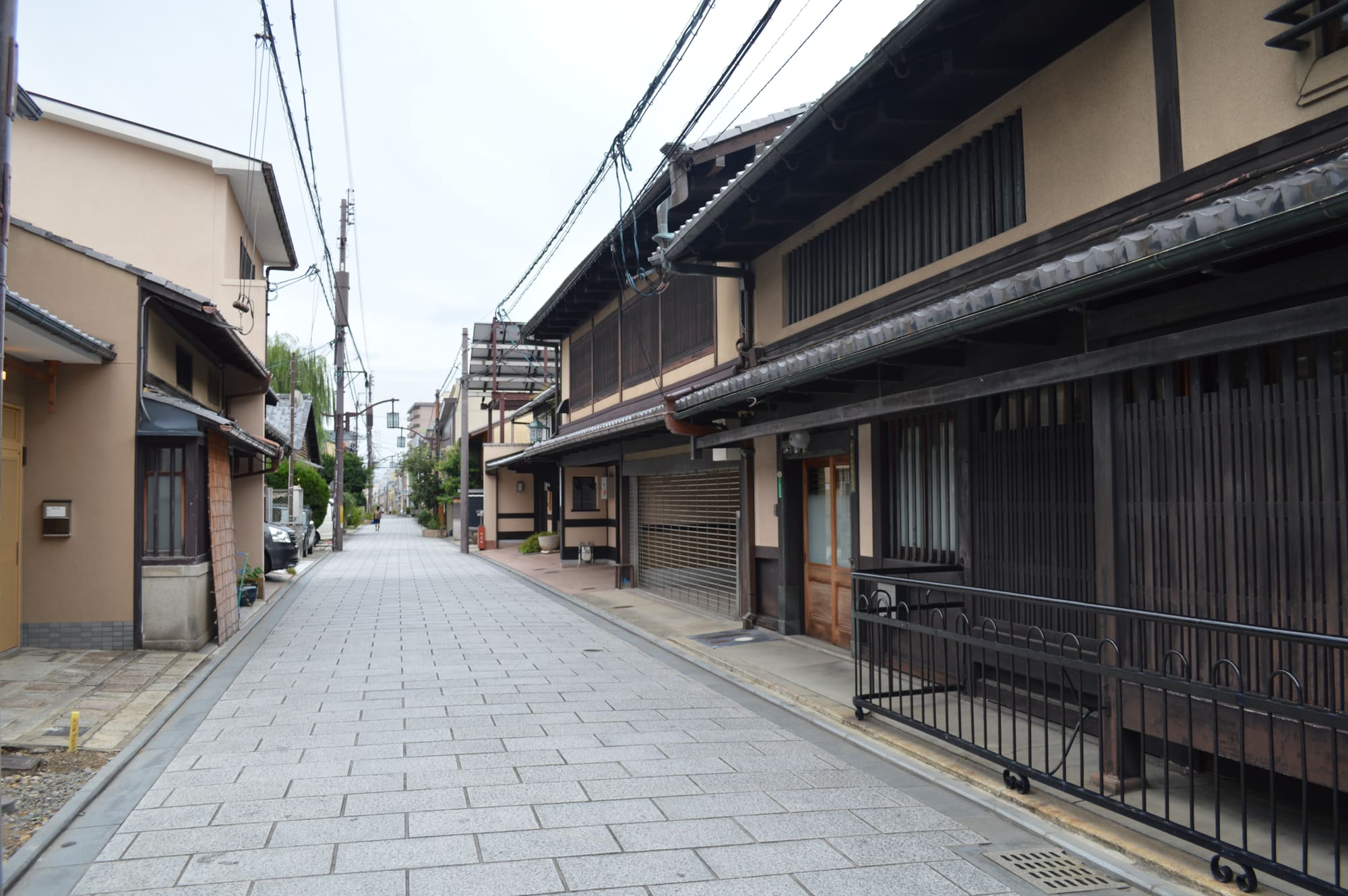 A quiet residential lane in Nishijin lined with dark-timbered machiya townhouses and latticed windows on an overcast day.